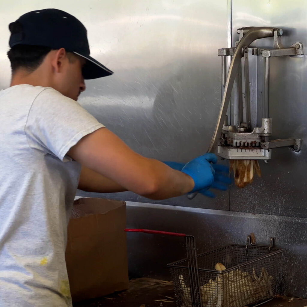 Employee cutting fresh potatoes in the hand-crank cutter at Gene and Jude’s for our Gene and Jude’s Chicago Fry Review.